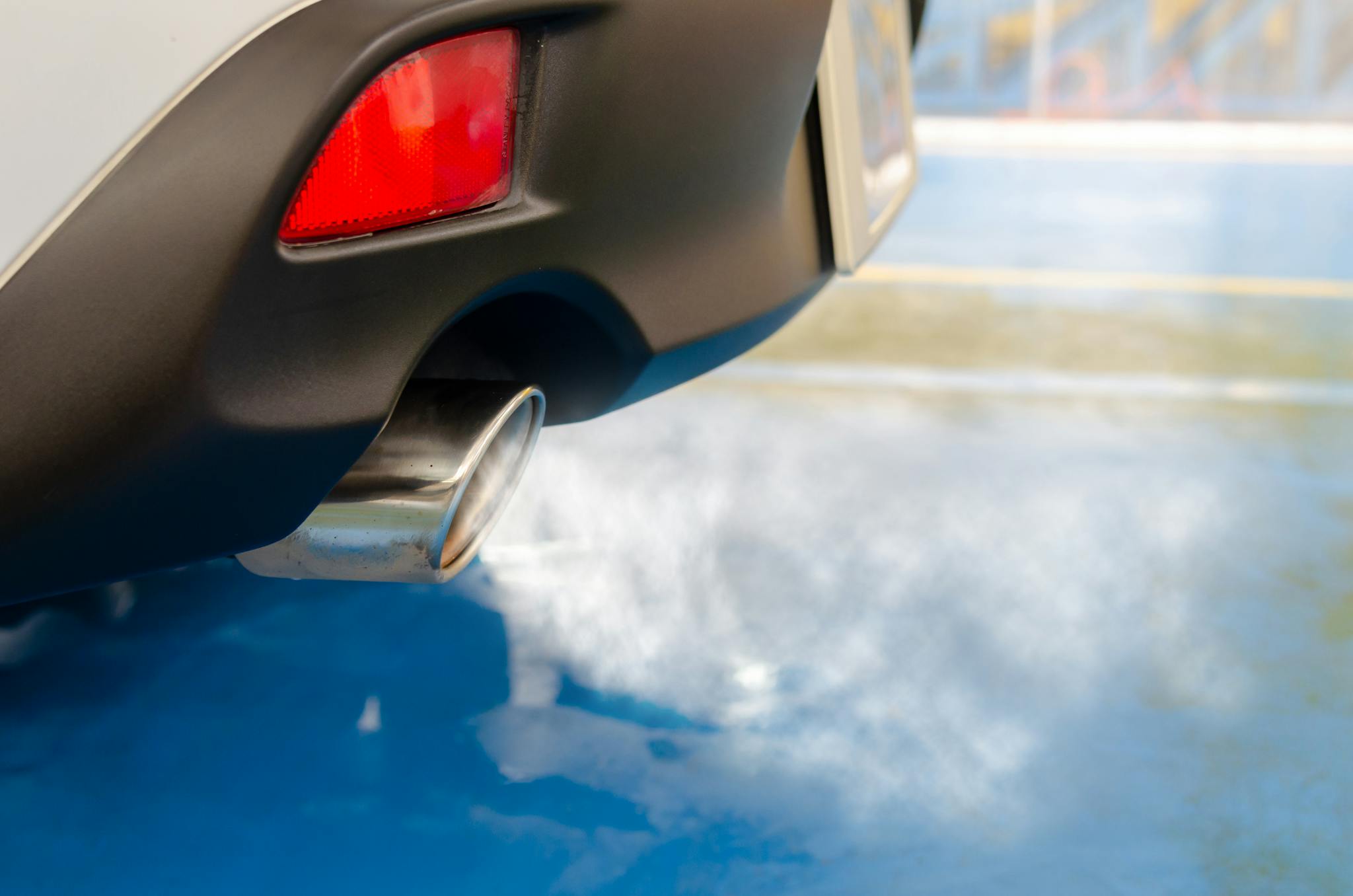 A close view of a car's exhaust pipe emitting smoke on a sunny day, highlighting pollution.