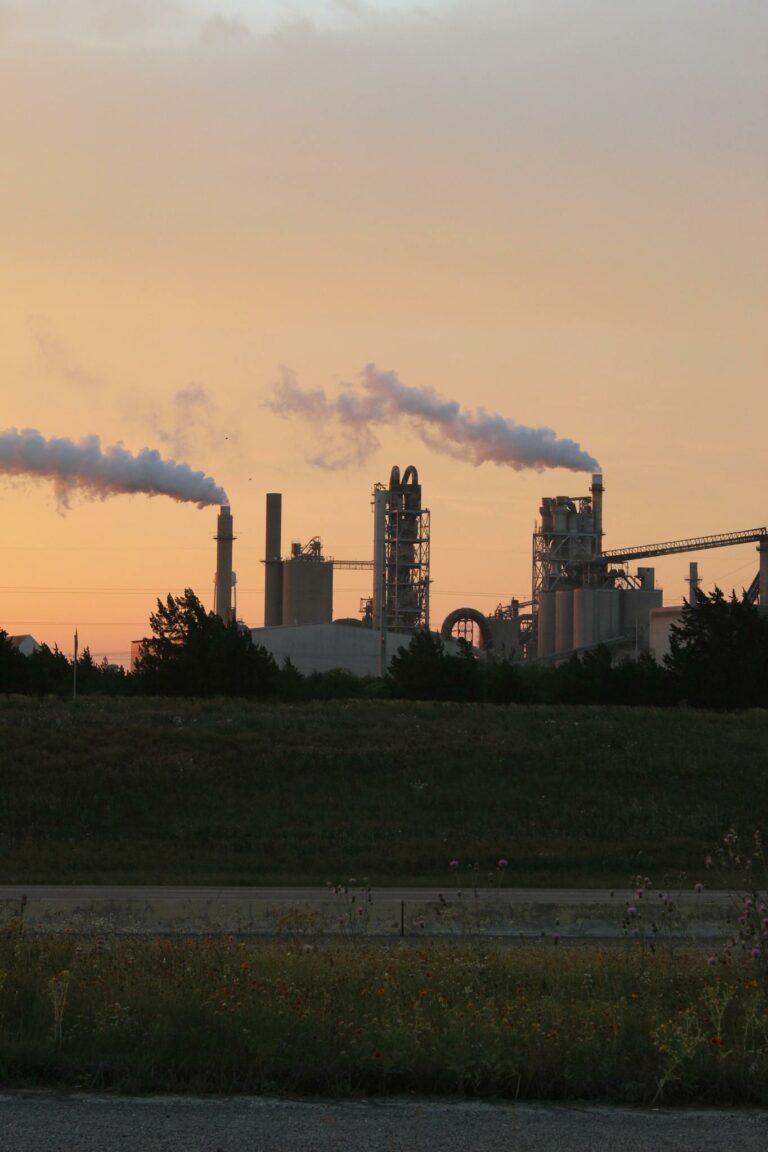 Factory chimneys releasing smoke during a vibrant sunset, highlighting industrial pollution.