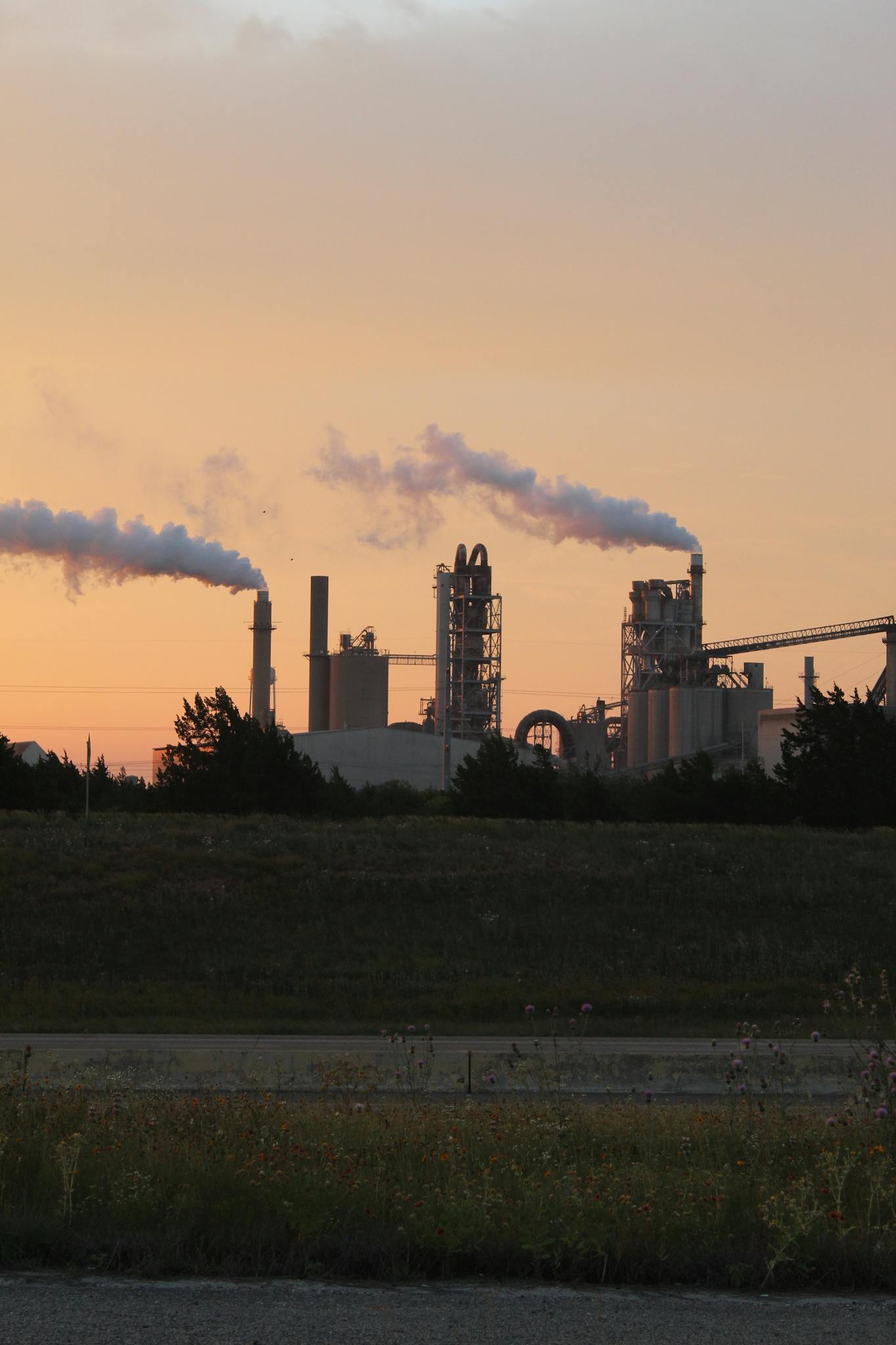 Factory chimneys releasing smoke during a vibrant sunset, highlighting industrial pollution.